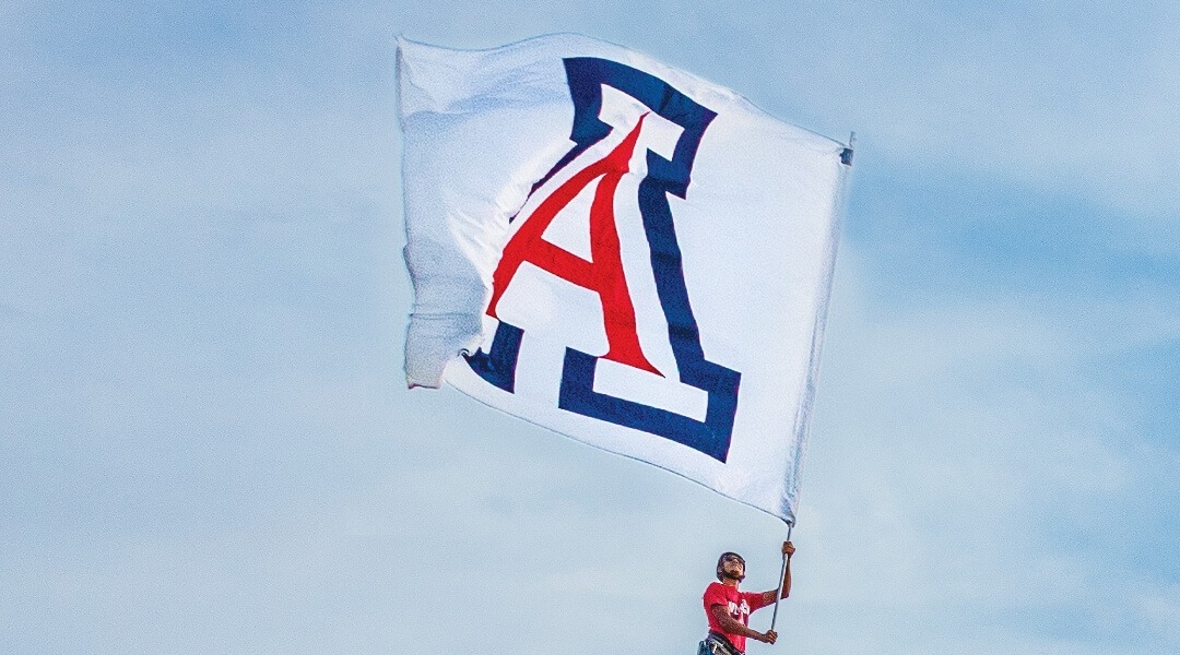 student waving flag with large University of Arizona logo